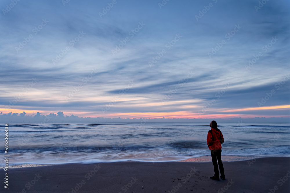 A woman standing by the ocean after sunset. Long exposure. North Holland dune reserve, Egmond aan Zee, Netherlands.