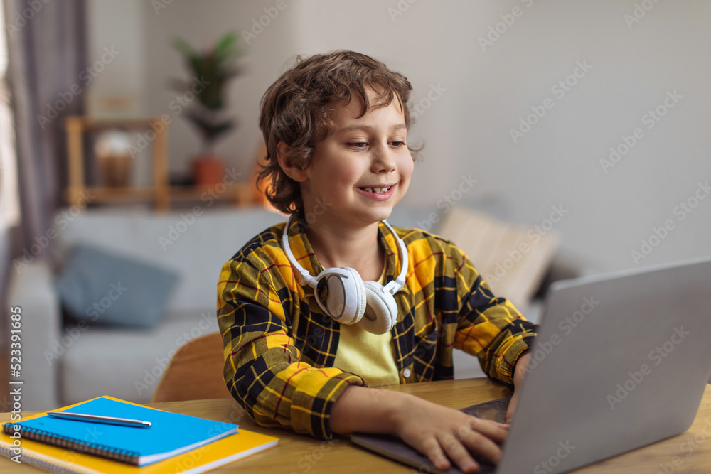 Positive little schoolboy typing on laptop, doing home task or watching online lesson, free space Positive little schoolboy typing on laptop, doing home task or watching online lesson, free space
