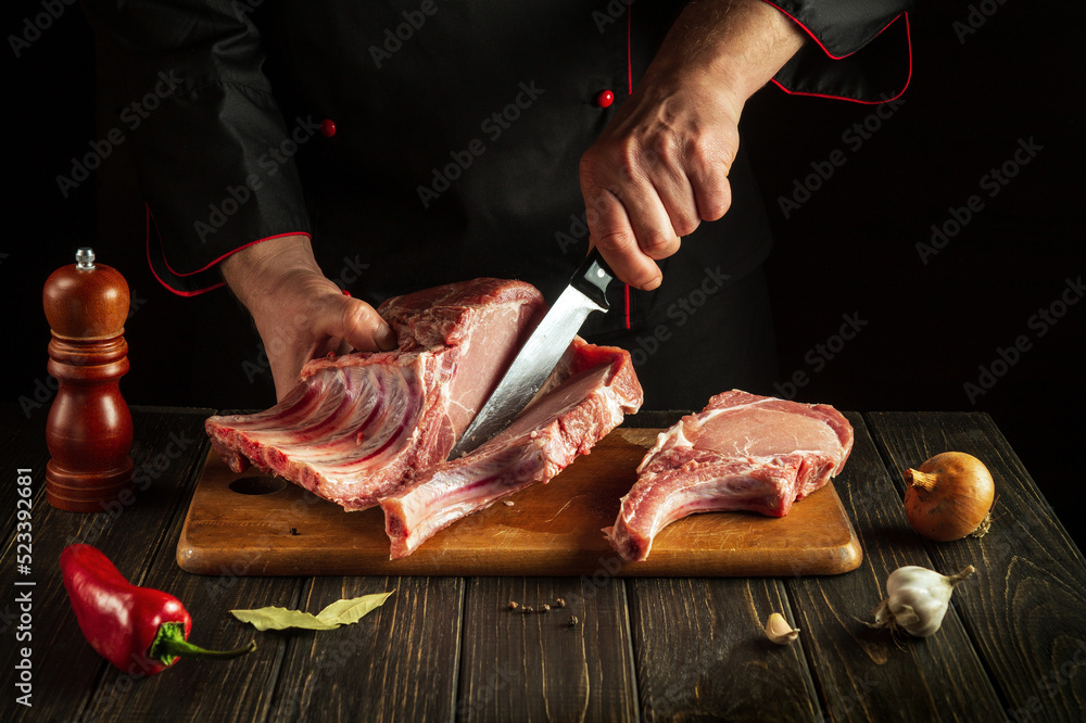 Cook or butcher cuts raw ribs on a cutting board before preparing a meat dish.. Hotel Recipe Idea