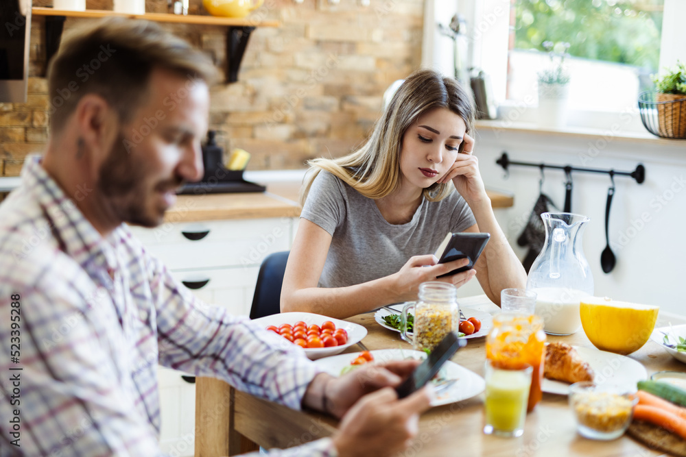 Young  couple using cell phones during breakfast at home