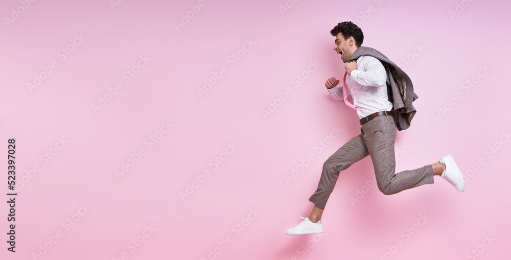 Excited man in shirt and tie carrying jacket on shoulder while jumping against pink background