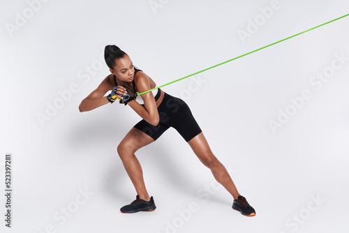 Concentrated young woman exercising with elastic resistance band against white background