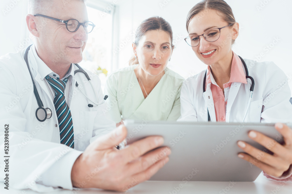 Team of doctors in meeting discussing a case looking at technology Team of doctors in meeting discussing a case looking at technology