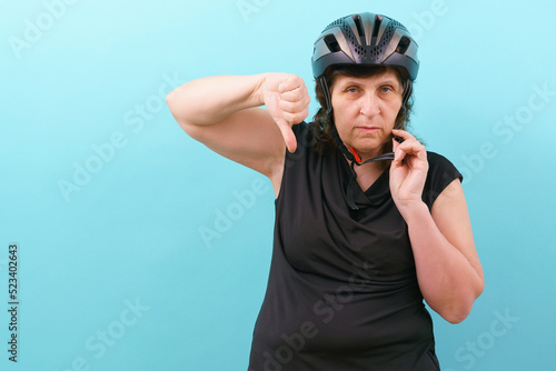 An upset woman wearing a bicycle helmet shows his thumb down on a blue background. Insurance. Injury. Protect. Secure. Protective. Perfect. Cycle. Express. Accident. Guard. Hobbies. Tool. Protector