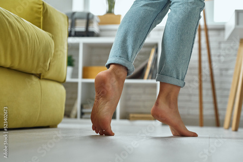 Close-up of barefoot woman walking on wooden floor at home