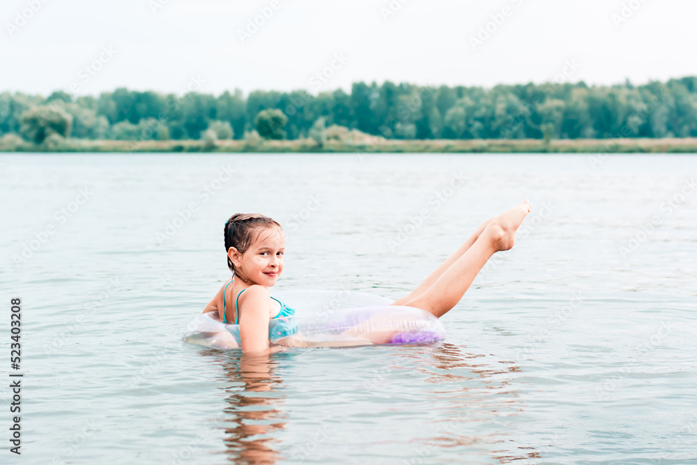 A cheerful girl swims on an inflatable ring in the river and stretches her legs. Local tourism. Summer vacation