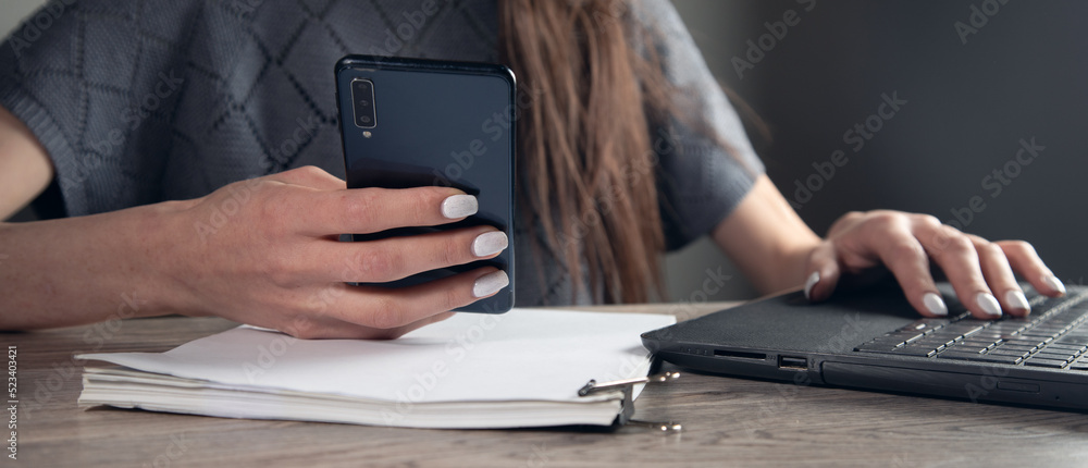 Business woman hand uses a mobile phone and works in a laptop computer Business woman hand uses a mobile phone and works in a laptop computer