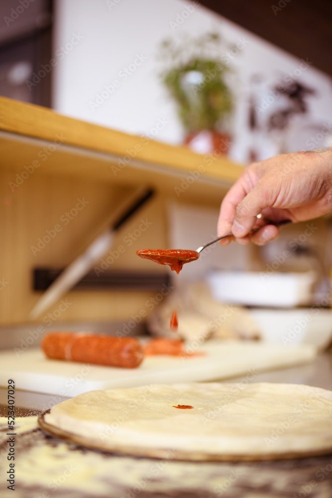 Fototapeta premium Faceless shot of chef pouring red sauce on pizza dough in cafe kitchen 