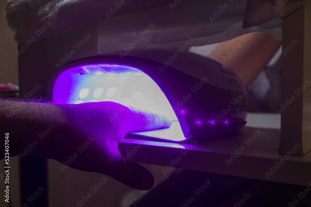 Client in manicure salon dryes gel polished nails in UV light lamp. Beauty salon and beautician appointment concept. Client in manicure salon dryes gel polished nails in UV light lamp. Beauty salon and beautician appointment concept.