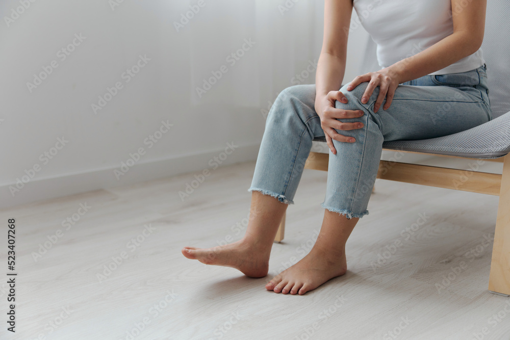 Meniscus. Closeup shot of pain leg knee suffering tanned beautiful young Asian woman touch injured knee at home interior living room. Injuries Poor health Illness concept. Cool offer Banner Meniscus. Closeup shot of pain leg knee suffering tanned beautiful young Asian woman touch injured knee at home interior living room. Injuries Poor health Illness concept. Cool offer Banner