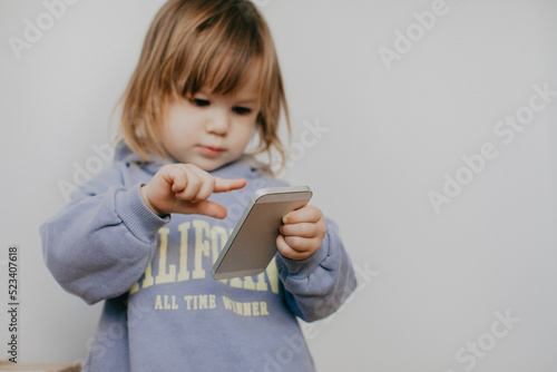 Little girl in violet hoodie using a phone on white background 
