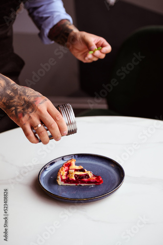 Cropped view of tattooed chef holding powdered sugar near cherry pie 