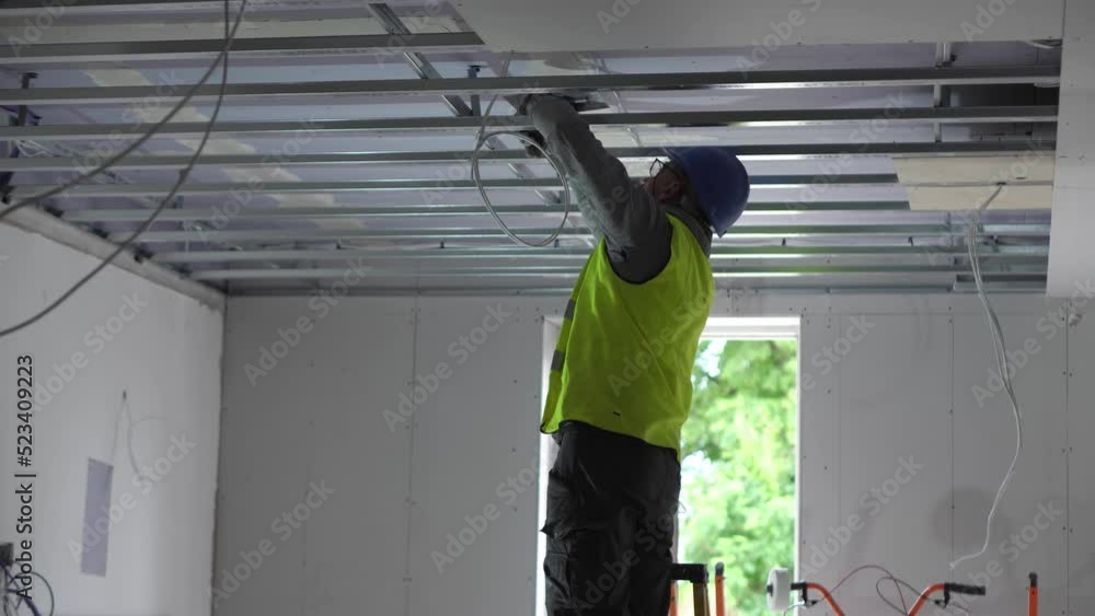 Hard male work on construction site. Two professional workers in special uniforms Contractors Safety Hats repairing ceiling wall inside building. Builders' equipment at workplace. industrial premises Hard male work on construction site. Two professional workers in special uniforms Contractors Safety Hats repairing ceiling wall inside building. Builders' equipment at workplace. industrial premises