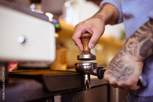 Partial view of tattooed barista pressing coffee in holder in cafe 