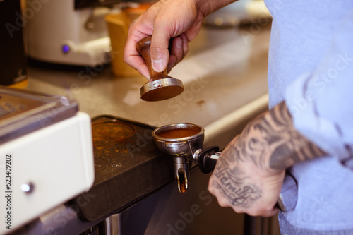 Partial view of tattooed barista holding coffee holder and press in cafe 