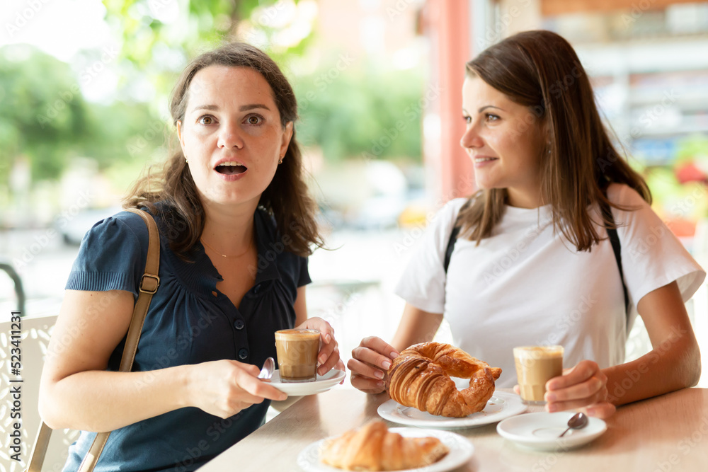 Two beautiful women sit at table in cafe with coffee and croissants. High quality photo