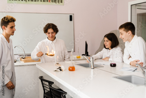 Chemistry lesson in labaratory. Education online in class with group of pupils studying on laptop  smiling and having fun together.