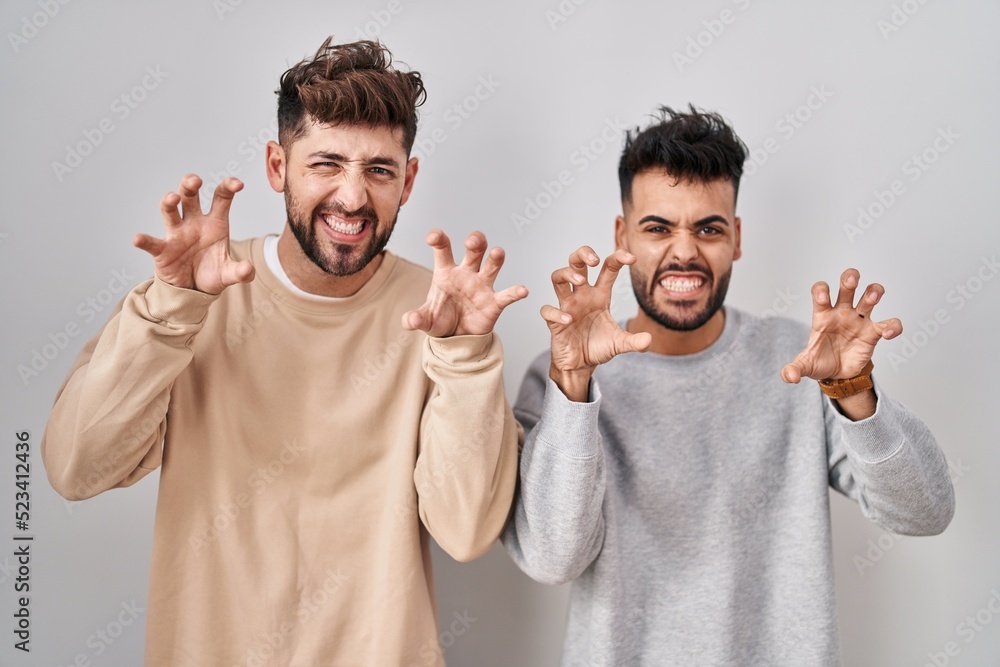 Young homosexual couple standing over white background smiling funny doing claw gesture as cat, aggressive and sexy expression Young homosexual couple standing over white background smiling funny doing claw gesture as cat, aggressive and sexy expression