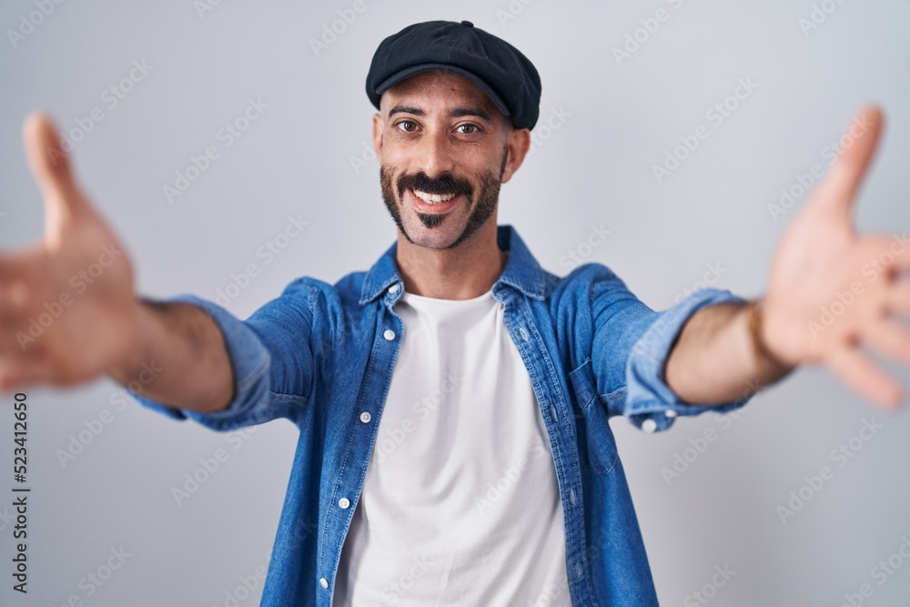 Hispanic man with beard standing over isolated background looking at the camera smiling with open arms for hug. cheerful expression embracing happiness. Hispanic man with beard standing over isolated background looking at the camera smiling with open arms for hug. cheerful expression embracing happiness.