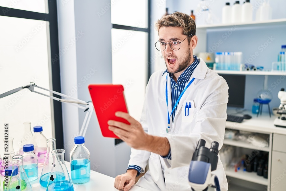Hispanic man with beard working at scientist laboratory doing video call scared and amazed with open mouth for surprise, disbelief face Hispanic man with beard working at scientist laboratory doing video call scared and amazed with open mouth for surprise, disbelief face