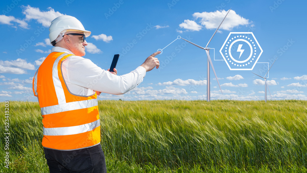 Engineer works at wind farm. Man technician with wind turbines. Worker in uniform power plant engineer. Man stretches hand towards windmills. World Energy consumption concept. Wind turbines in field