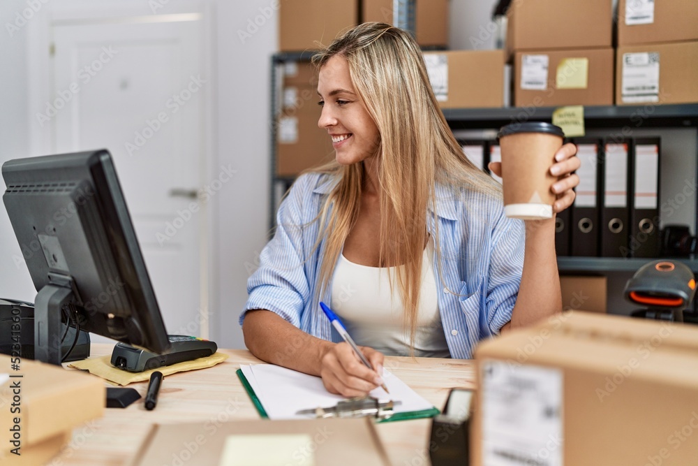 Young blonde woman ecommerce business worker drinking coffee working at office