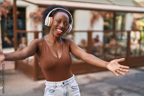 African woman with curly hair outdoors at the city wearing headphones celebrating crazy and amazed for success with open eyes screaming excited.