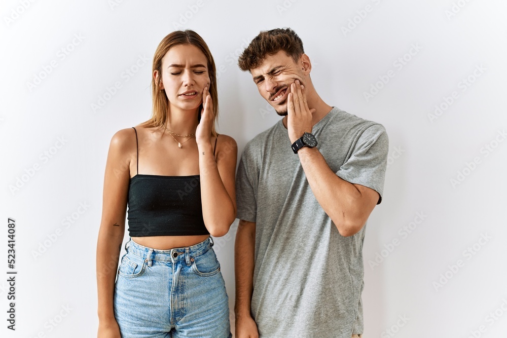 Naklejka premium Young beautiful couple standing together over isolated background touching mouth with hand with painful expression because of toothache or dental illness on teeth. dentist