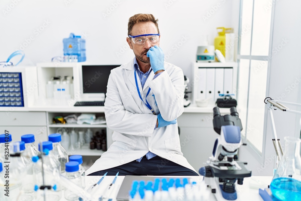 Middle age man working at scientist laboratory looking stressed and nervous with hands on mouth biting nails. anxiety problem. Middle age man working at scientist laboratory looking stressed and nervous with hands on mouth biting nails. anxiety problem.