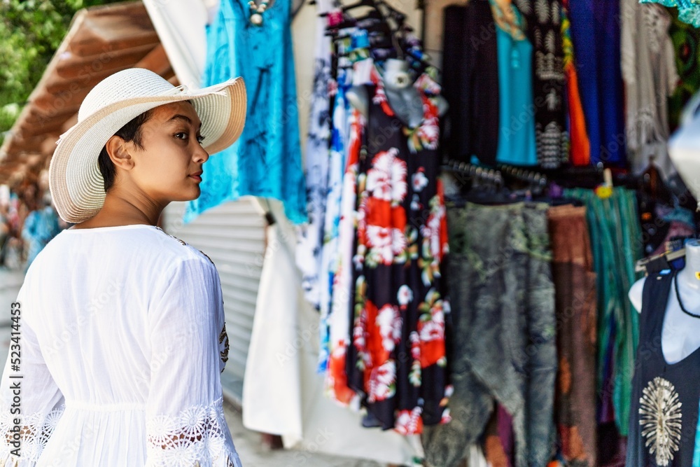 Young hispanic woman wearing summer hat shopping at street market