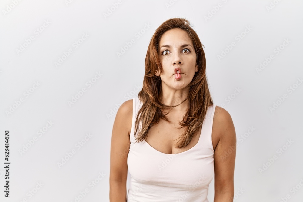 Middle age hispanic woman standing over isolated background making fish face with lips, crazy and comical gesture. funny expression. Middle age hispanic woman standing over isolated background making fish face with lips, crazy and comical gesture. funny expression.