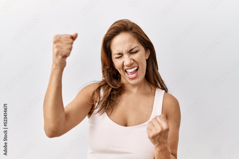 Fototapeta premium Middle age hispanic woman standing over isolated background very happy and excited doing winner gesture with arms raised, smiling and screaming for success. celebration concept.