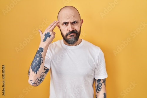 Canvas Print Young hispanic man with tattoos standing over yellow background shooting and killing oneself pointing hand and fingers to head like gun, suicide gesture