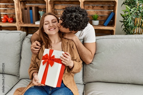 Young couple smiling happy sitting on the sofa surprise with anniversary gift at home.