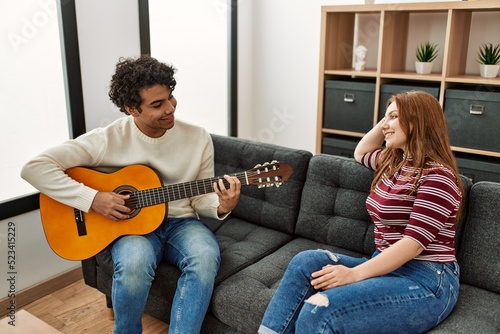 Young couple smiling happy playing classical guitar sitting on the sofa at home.