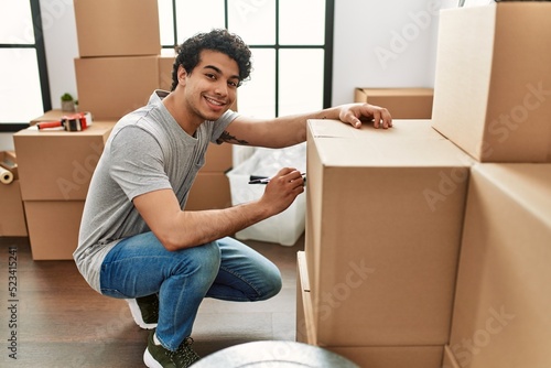 Young hispanic man smiling happy packing boxes at new home. © Krakenimages.com