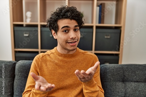 Young hispanic man smiling happy and speaking sitting on the sofa at home. photo