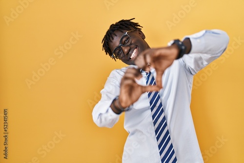 African man with dreadlocks standing over yellow background smiling in love doing heart symbol shape with hands. romantic concept.