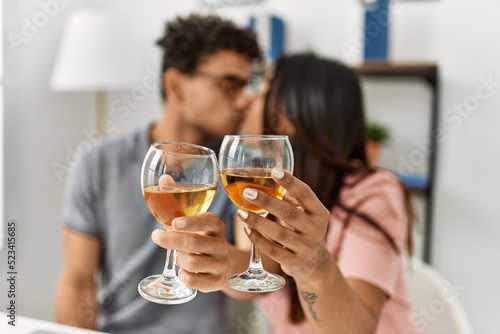 Young latin couple kissing and toasting with wine sitting on the table at home.