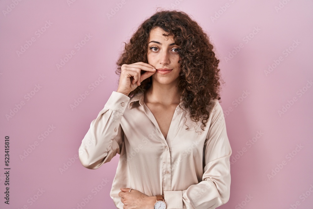 Hispanic woman with curly hair standing over pink background mouth and lips shut as zip with fingers. secret and silent, taboo talking Hispanic woman with curly hair standing over pink background mouth and lips shut as zip with fingers. secret and silent, taboo talking