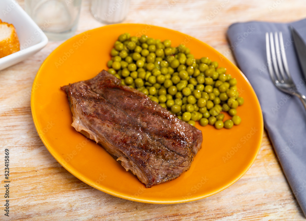 Grilled beef steak garnished with peas. Roasted beefsteak, main dish on table.