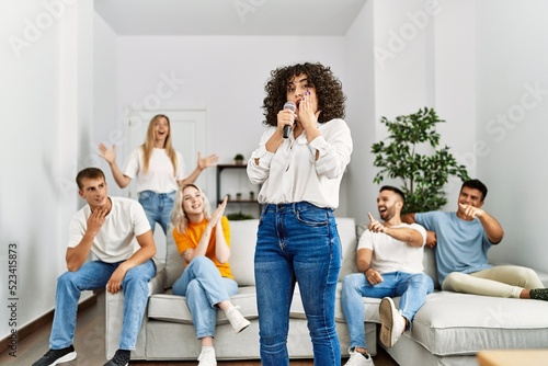 Group of young friends having party singing song using microphone at home.