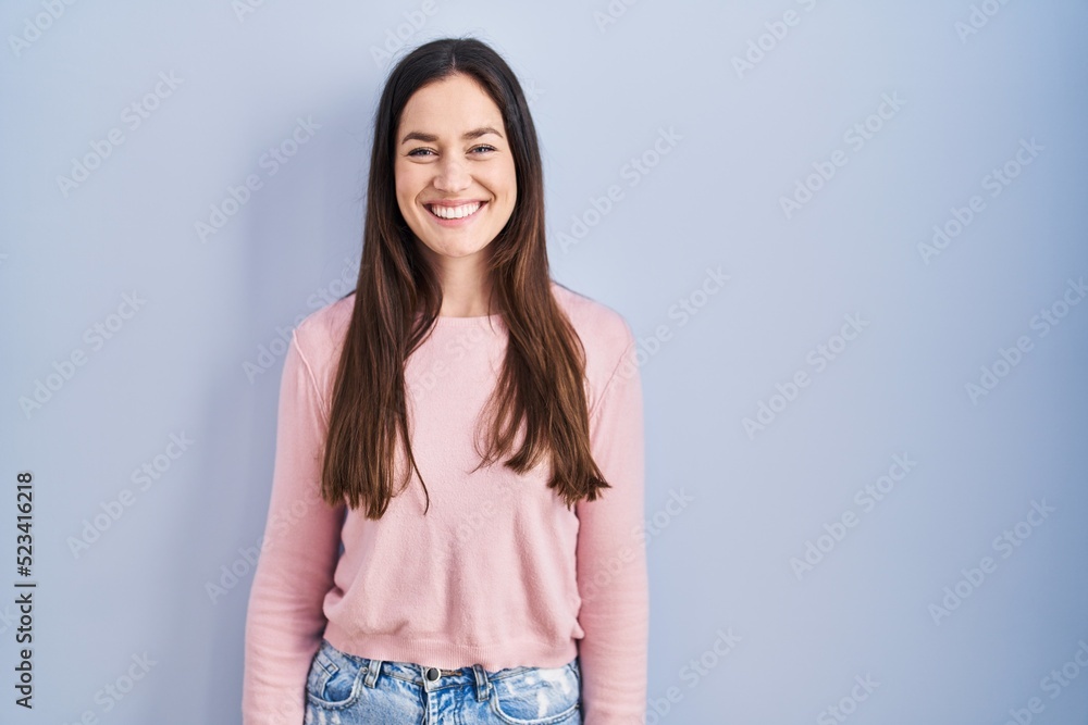 Young brunette woman standing over blue background with a happy and cool smile on face. lucky person. Young brunette woman standing over blue background with a happy and cool smile on face. lucky person.
