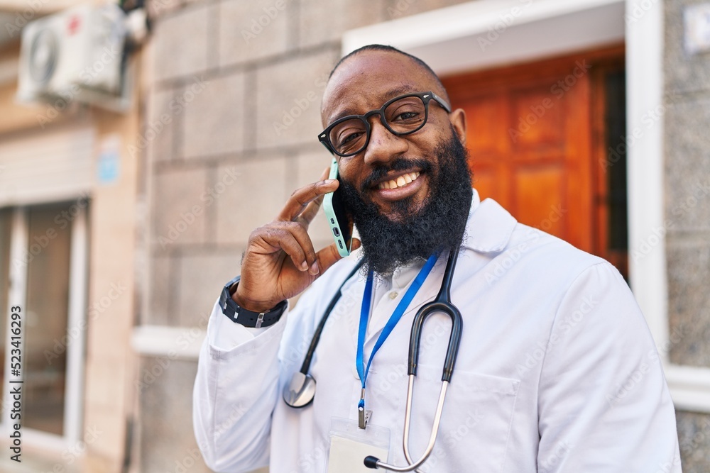 Young african american man wearing doctor uniform using smartphone at hospital Young african american man wearing doctor uniform using smartphone at hospital