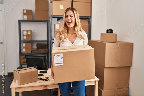 Young blonde woman working at small business ecommerce holding big box winking looking at the camera with sexy expression, cheerful and happy face. © Krakenimages.com