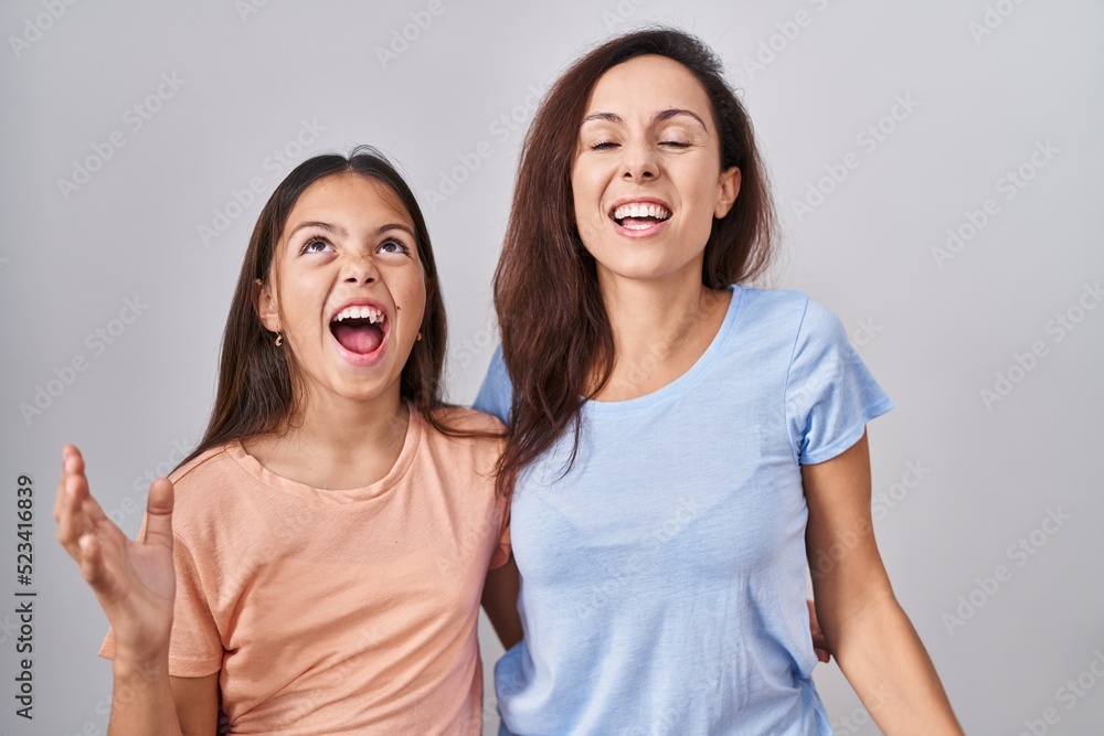 Young mother and daughter standing over white background crazy and mad shouting and yelling with aggressive expression and arms raised. frustration concept. Young mother and daughter standing over white background crazy and mad shouting and yelling with aggressive expression and arms raised. frustration concept.