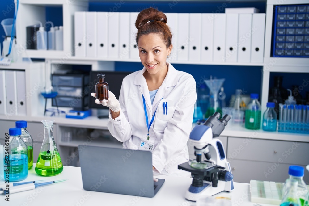 Young woman scientist using laptop holding bottle at laboratory Young woman scientist using laptop holding bottle at laboratory