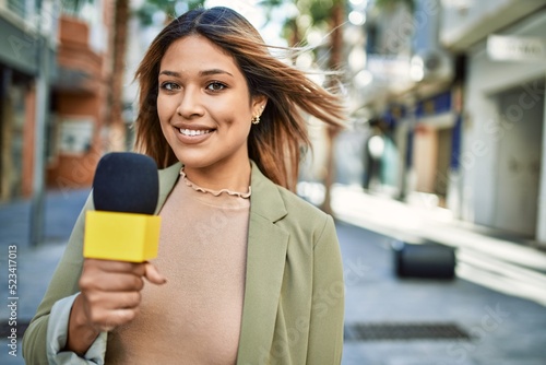 Young latin woman smiling confident using microphone at street