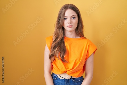 Caucasian woman standing over yellow background relaxed with serious expression on face. simple and natural looking at the camera.