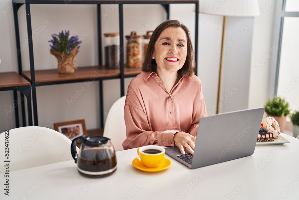 Middle age woman having breakfast using laptop sitting on table at home Middle age woman having breakfast using laptop sitting on table at home